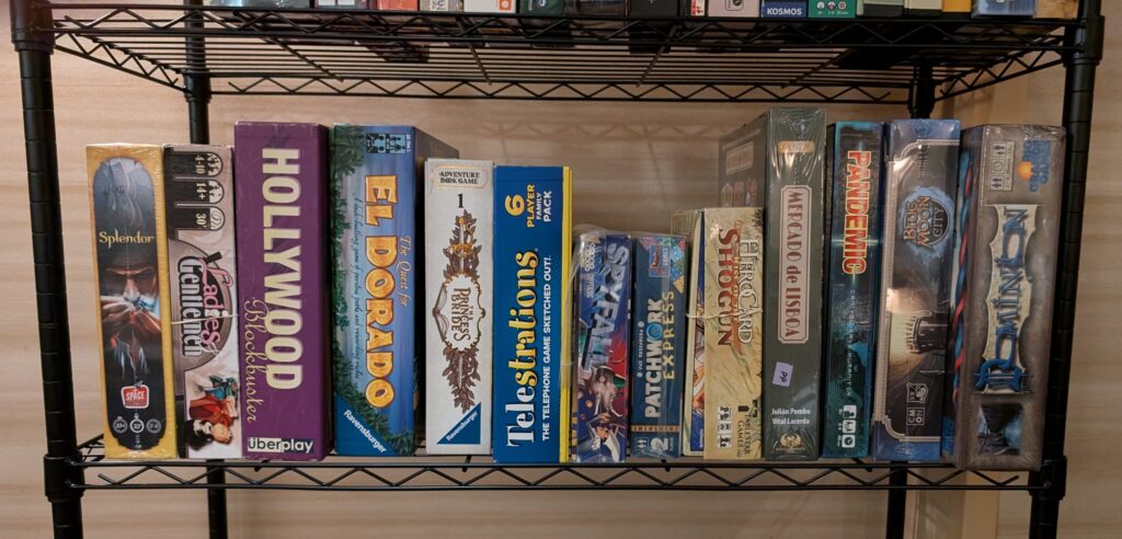 A line of boardgames on a wire shelf.